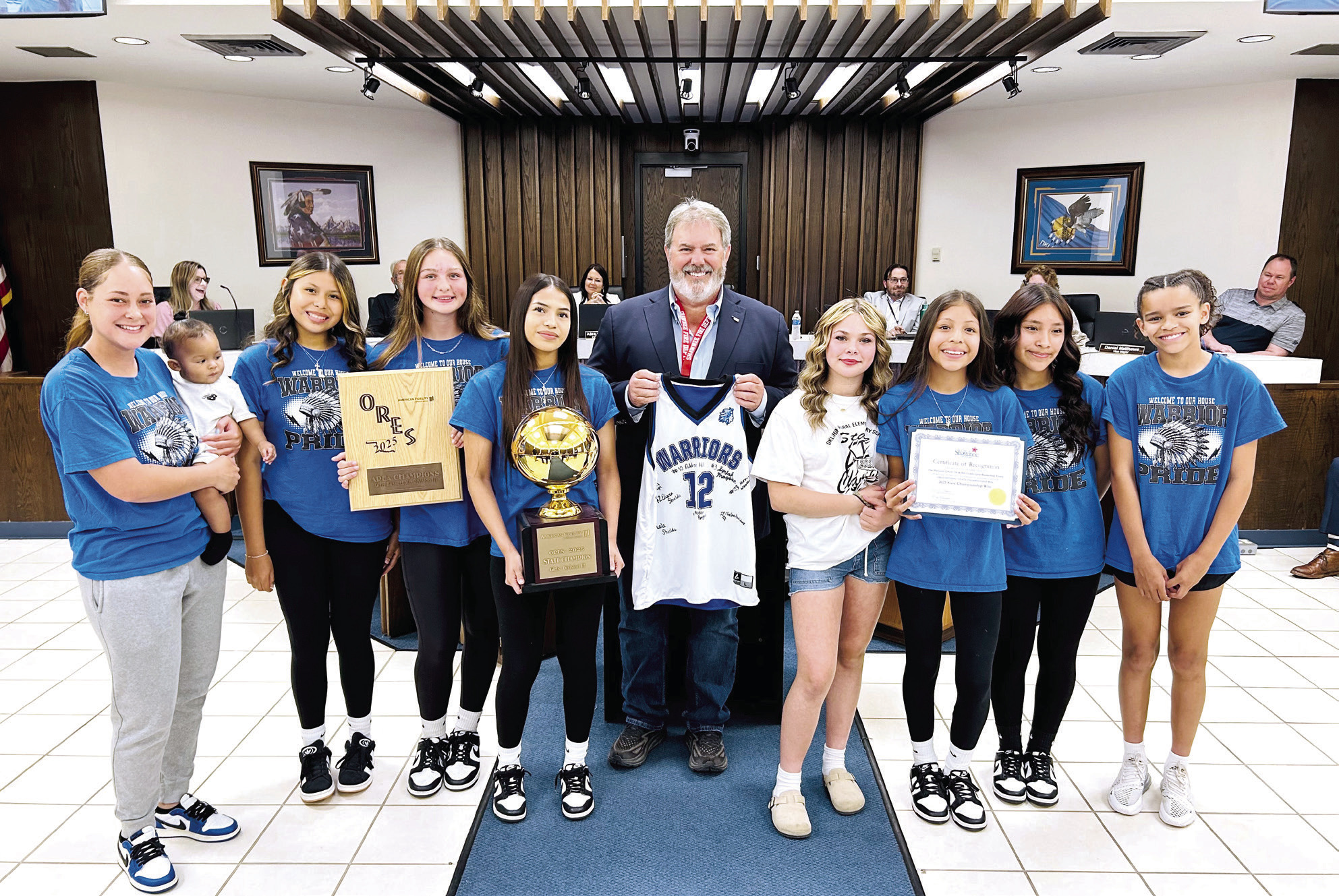 On behalf of the Shawnee Board of City Commissioners, Mayor Eric Stephens presented a Certificate of Recognition to the Pleasant Grove Girls Basketball team who won their second consecutive ORES Division III Championship. The Lady Warriors then presented Stephens with a signed jersey. Shawnee High School Girls Swim Team was also recognized for securing their fourth consecutive OSSAA 5A State Championship title. Both teams received a challenge coin from the Mayor. Photo provided by City of Shawnee