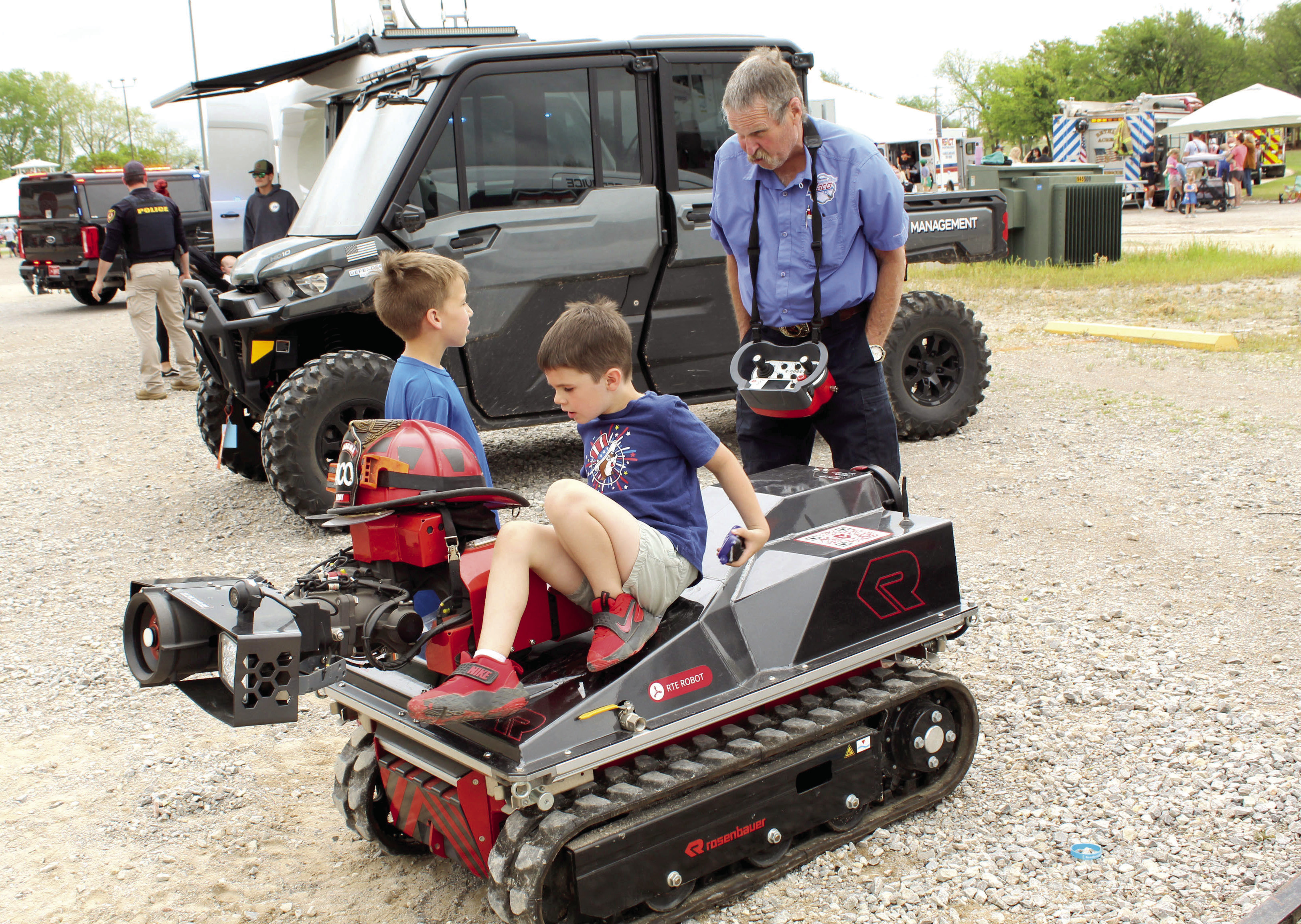 Hunter Elmore, 8, standing, talks with Rosenbauer dealer Mark Hardy about the remote control robot firefighter, as Troy Palmer, 5, sits on it, during Touch-A-Truck and Beyond, held at the CPN Festival Grounds on April 11 and organized by Pottawatomie County Emergency Management. Both boys are from Shawnee. Photos by Natasha Dunagan, Countywide & Sun