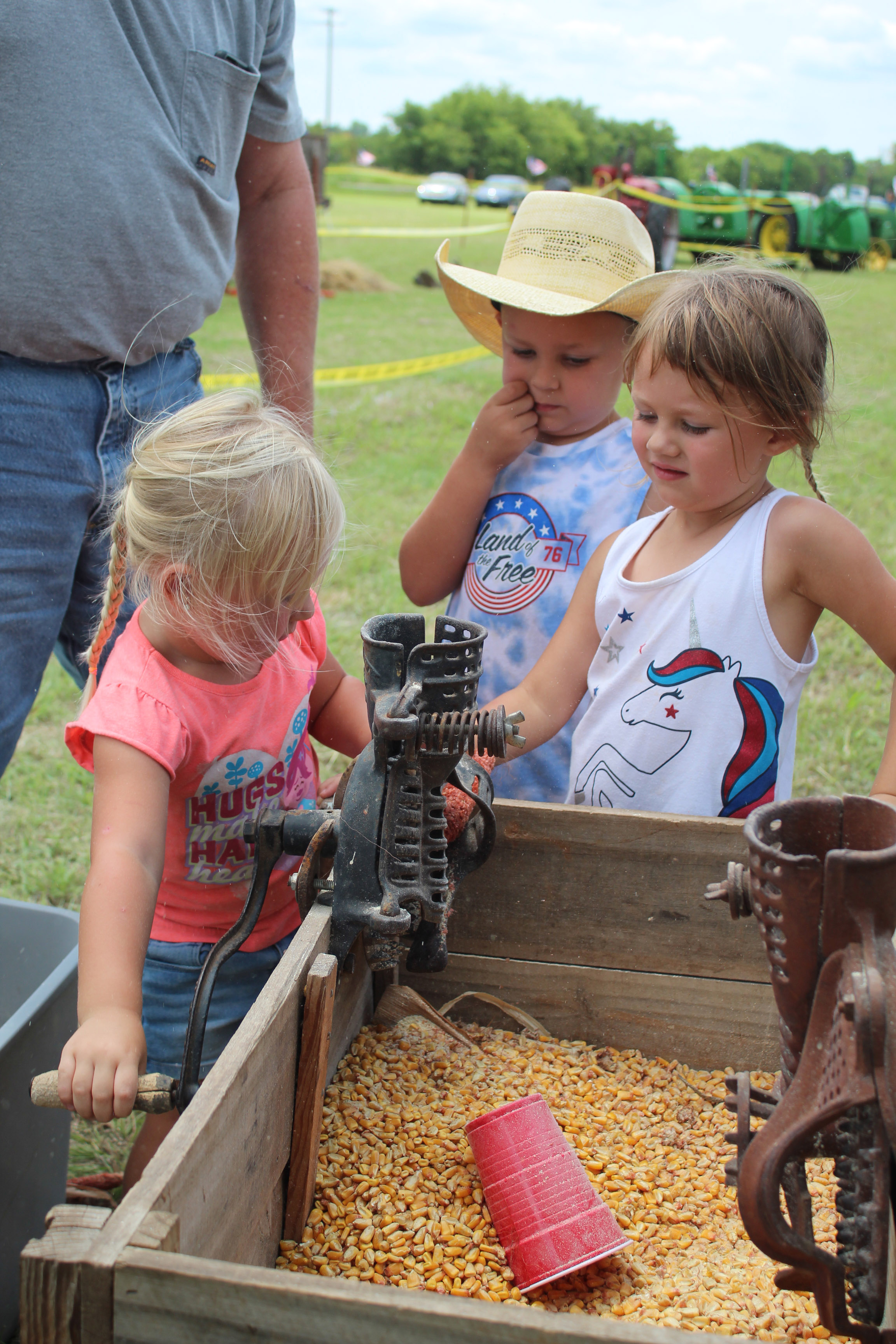 Lula Dailey, 2, turns a crank on a hand corn sheller owned by Mike Rooker of Dale, as Eli Dailey, 5, and Leila Dailey, 3, all of Earlsboro, watch during the Farming Heritage Festival at Shawnee Feed on June 17. Hosted by the Shawnee Tractor and Engine Club, the event is in its 24th year and also included several farming demonstrations, tractor pulling and an antique tractor parade on June 16 and 17. Countywide & Sun/Natasha Dunagan