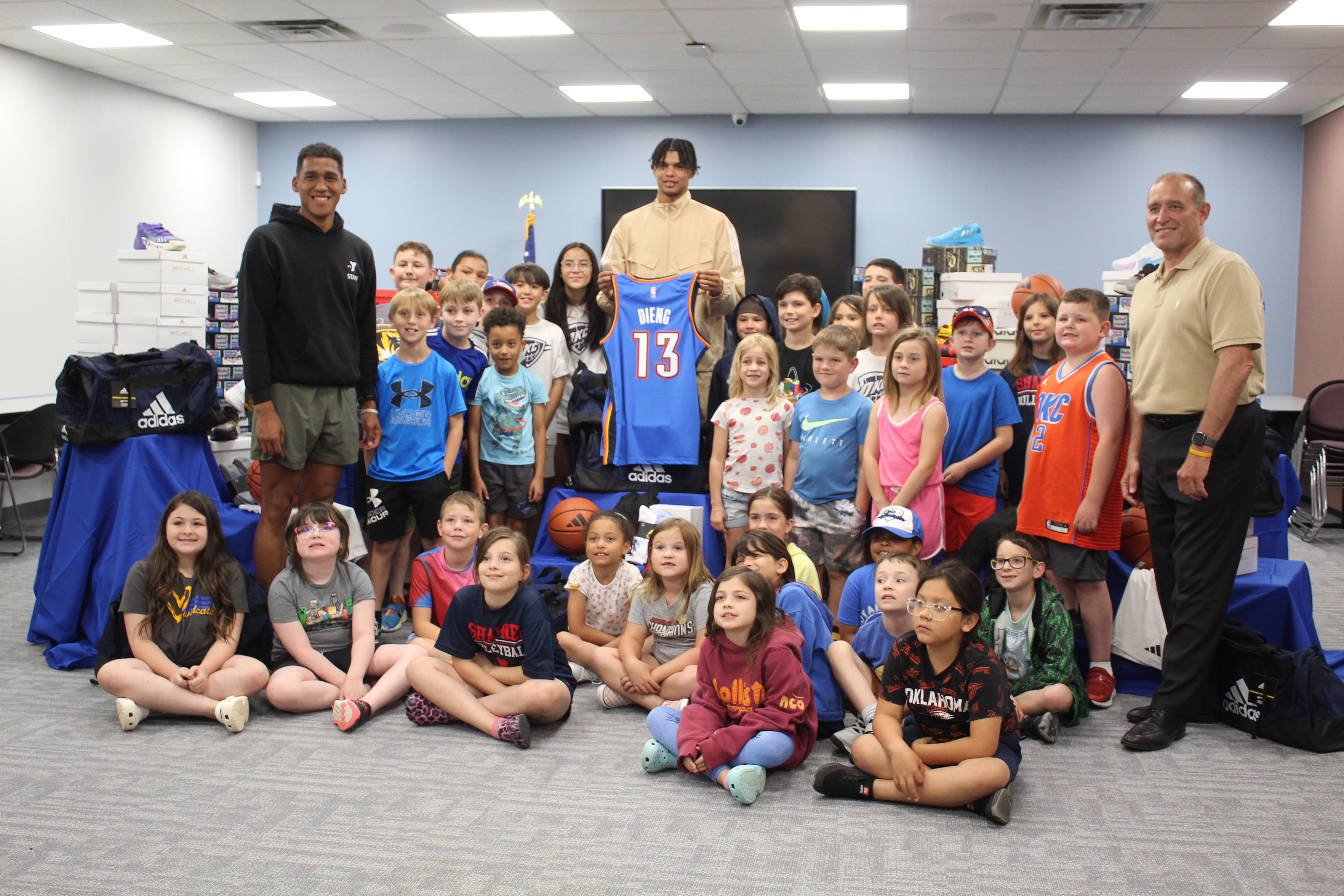 Oklahoma City Thunder Forward Ousmane Dieng, center; Shawnee YMCA Sports Director Brendon Johnson, far left; and YMCA CEO Mike Jobe, far right, pose with about 30 children from the YMCA Summer Camp, being held at Gordon Cooper Technology Center. According to a Thunder press release Thunder, Dieng, through a partnership with Adidas, donated shoes to Shawnee children who were affected by the April 19 tornadoes. YMCA Director of Operations Barbara Boise said 80 summer camp attendees will benefit.