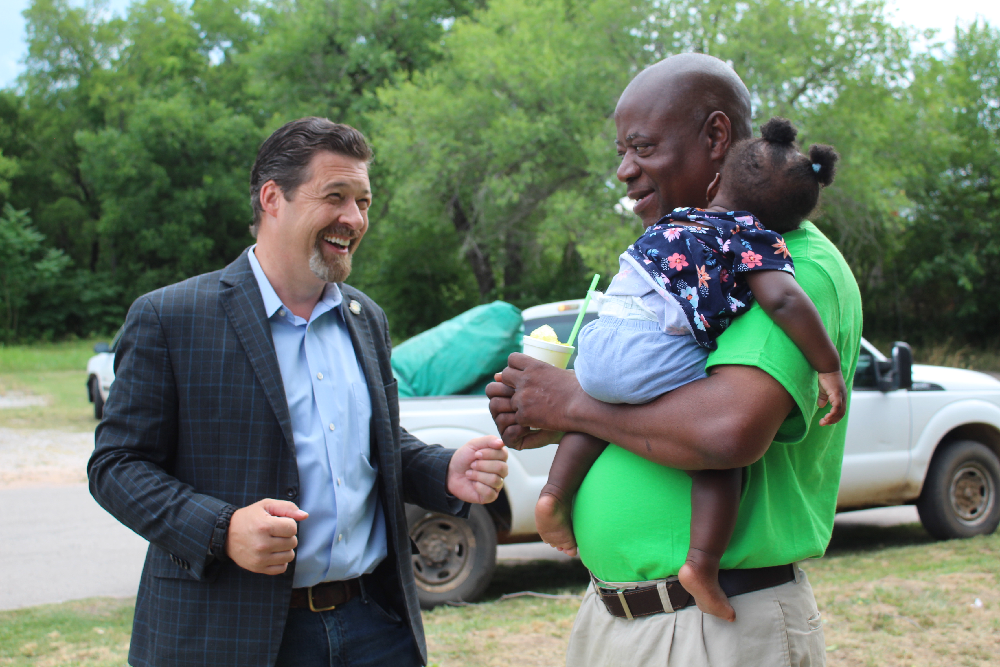 Epic Sno Cones owner David Henry, right, holds his sleeping granddaughter, Safiya Henry, 9 months, and eats a Mississippi Squirrel snow cone, as he talks with Oklahoma Senator Shane Jett on July 3. Shawnee’s oldest snow cone stand, at 722 S. Beard, was set to have their grand re-opening that day, but the electricity went off. They will announce when the event will be rescheduled.
