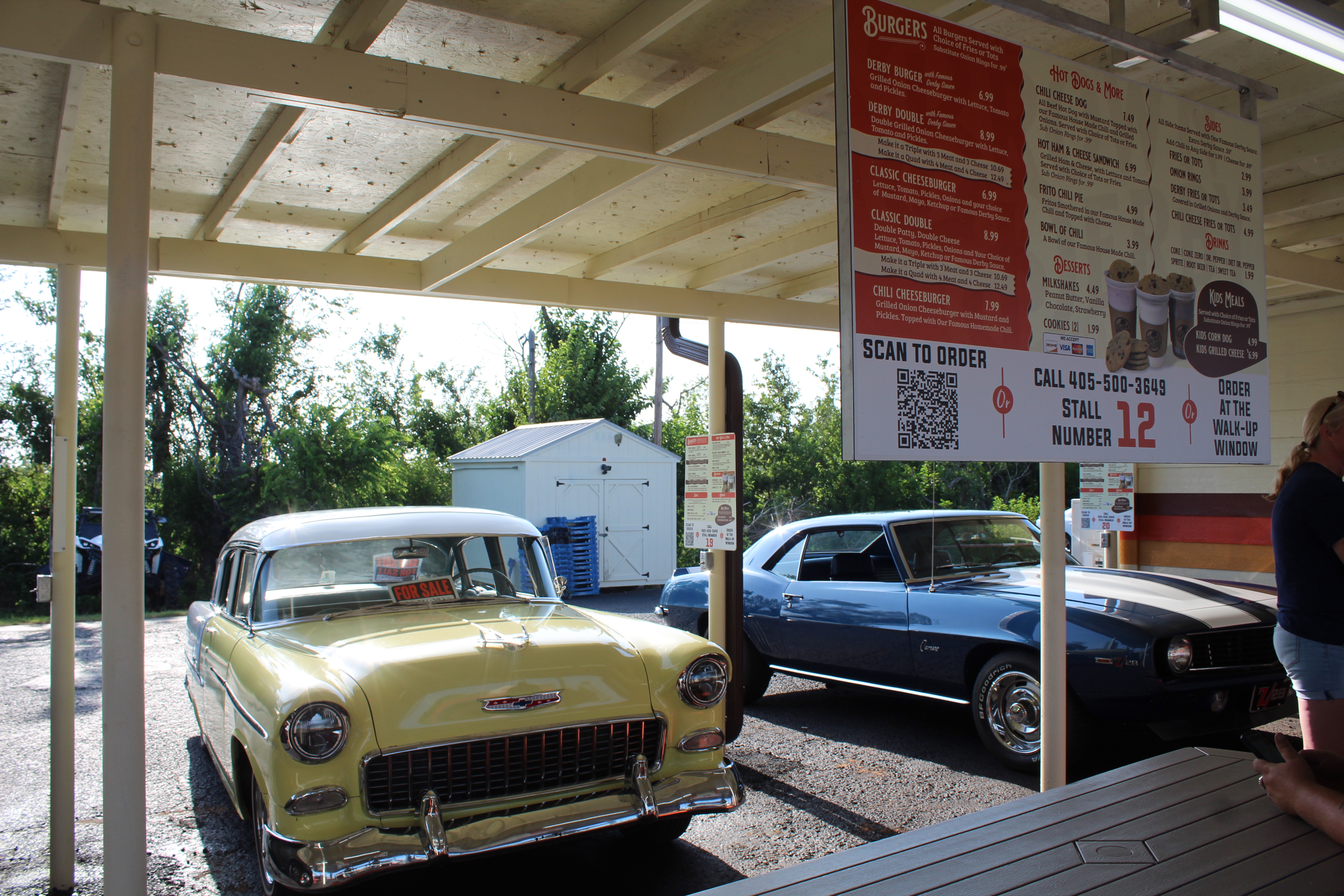 A 1955 Chevrolet Belair, owned by J.R. Lloyd of Shawnee, and a 1969 Chevrolet Camaro, belonging to Shane and Vivian Brown of Shawnee, were two of the vehicles at the monthly Cruise the Poo 2.0 on July 29. They met at The Brown Derby, which reopened on July 26 after recovering from tornado damage. Their original radios could not be replaced, so orders will now be taken using a QR Code, by phone or at the walk-up window, as seen on menus in front of each stall.