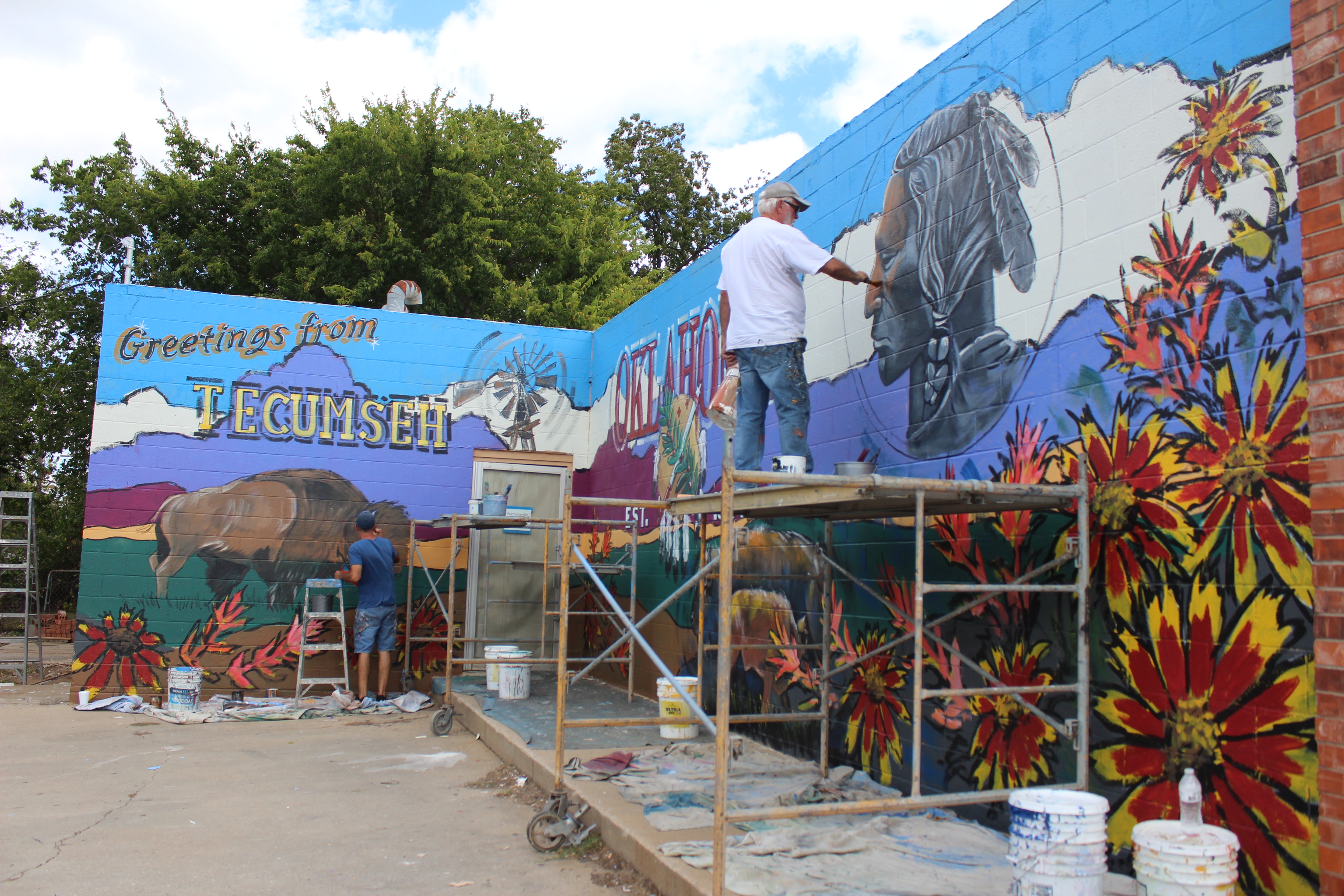 Bob Palmer, foreground, and Shane Cox work on a mural, Oct. 11, on the west side of the building at 421 E. Walnut in Tecumseh. The former laundromat next to Ma Beasley's Daylight Donuts is owned by Joshua and Katie Goodson, and will soon open as Affinity Corporation, a construction and design business. Katie Goodson said she wanted bright colors and Tecumseh and Oklahoma images, and she is happy with the result, which took two days to complete. 