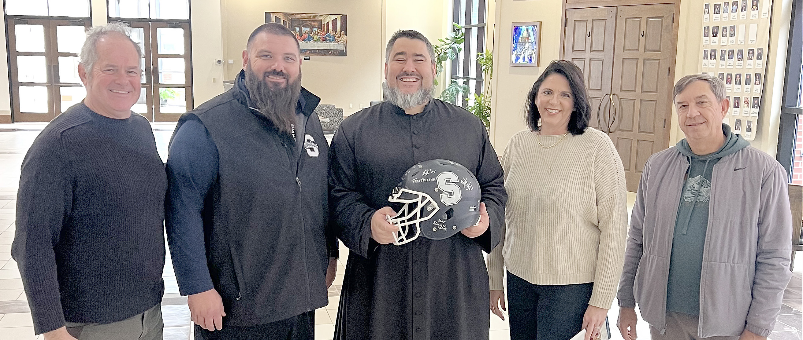 On Dec. 5, Shawnee Wolves Football Head Coach Jason Madonna presented St. Benedict's Church Very Rev. Christopher Brashears, pastor, and Danielle Roberts, office manager, with a helmet autographed by the football team players. See full cutline below.