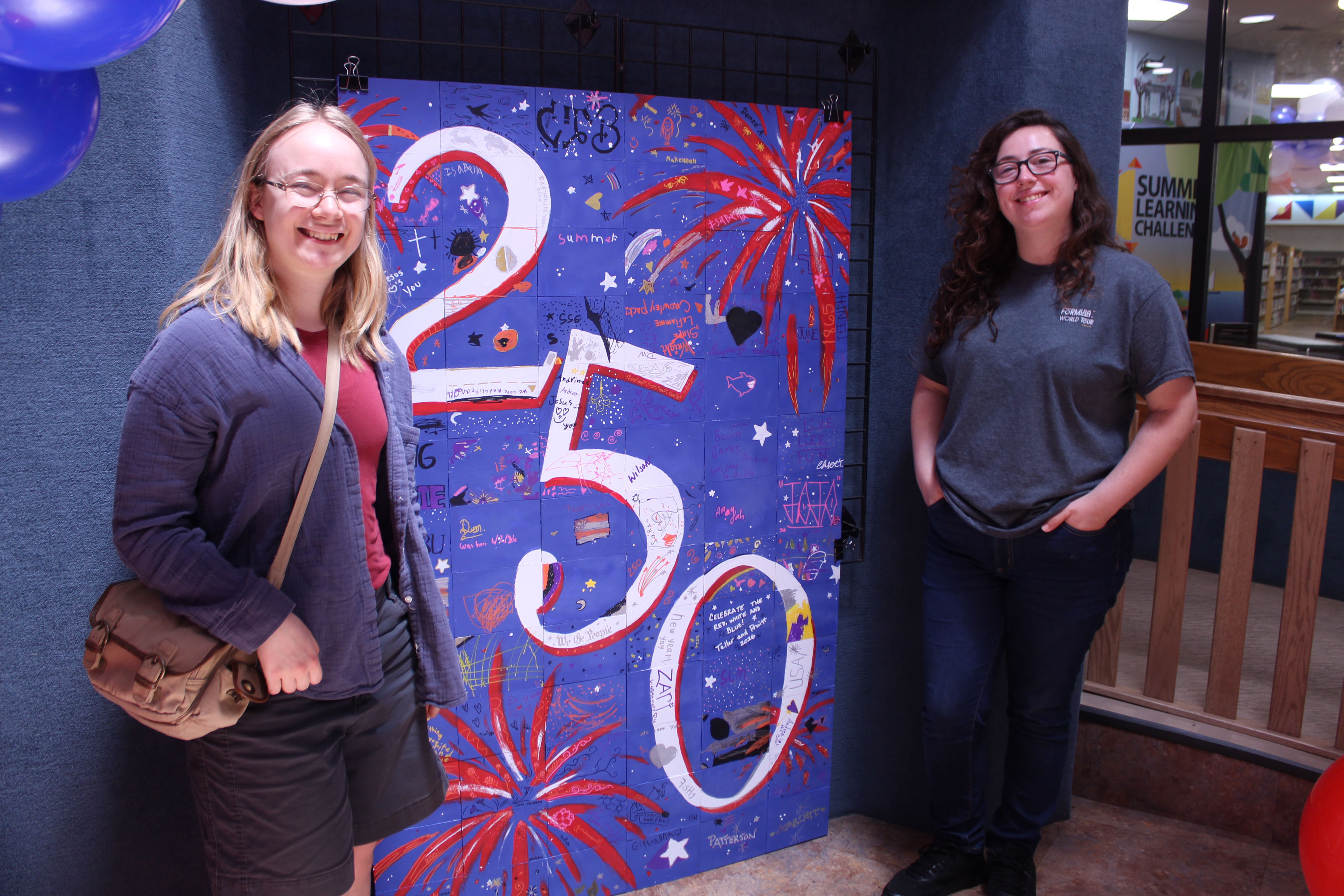 Oklahoma Baptist University graduates Linnea Malmberg, left, and Abigail Ryan pose by a community tile artwork, which they coordinated since May, during the "Pop In to Celebrate America's 250th Birthday with Popcorn and Ice Cream" event at Shawnee Public Library on June 29.  - Photos by Natasha Dunagan, Countywide & Sun