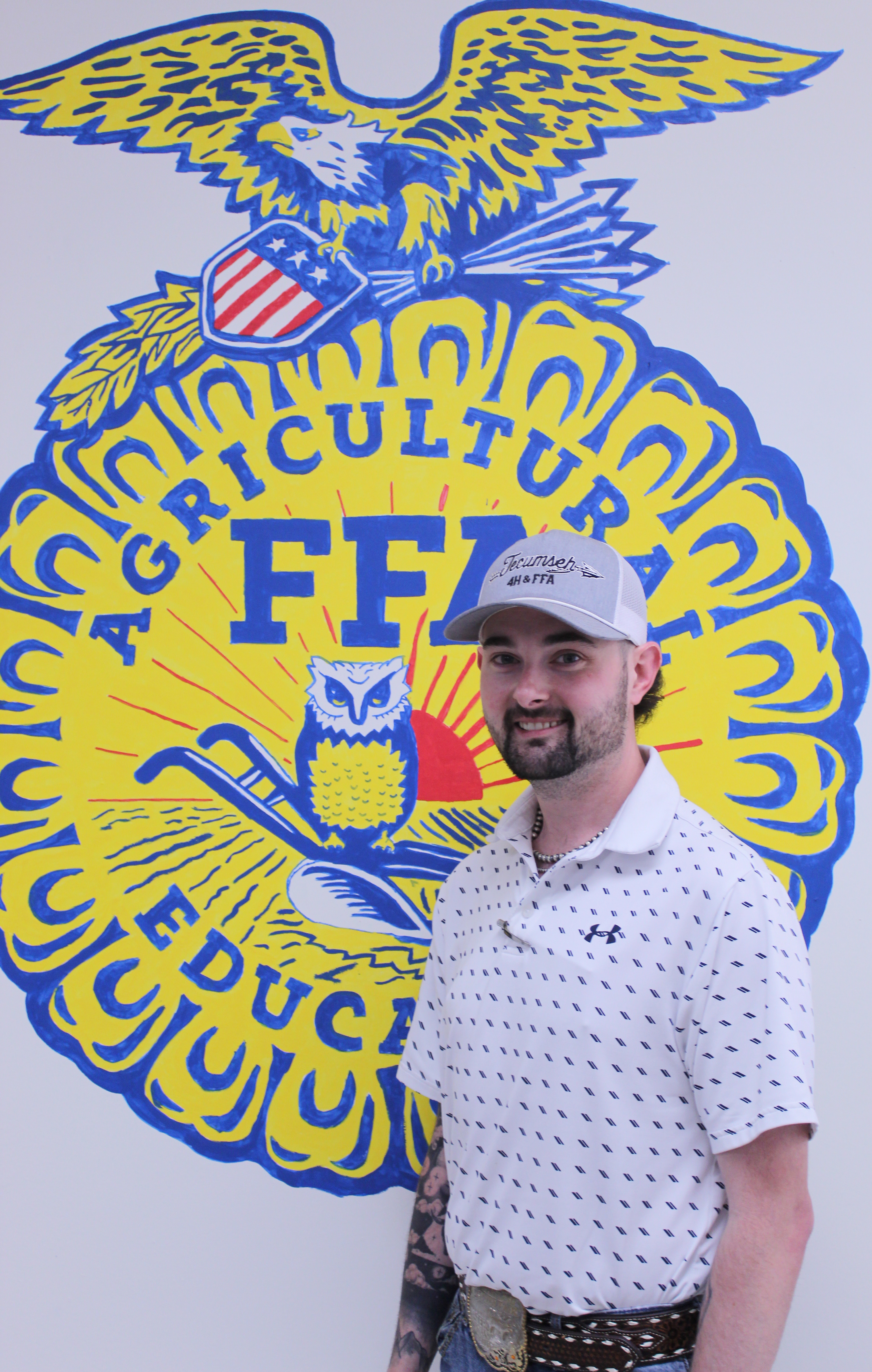 Chase Ferguson poses by the FFA logo that he and his students painted in his classroom at the THS Ag Building.  Photo by Natasha Dunagan, Countywide & Sun