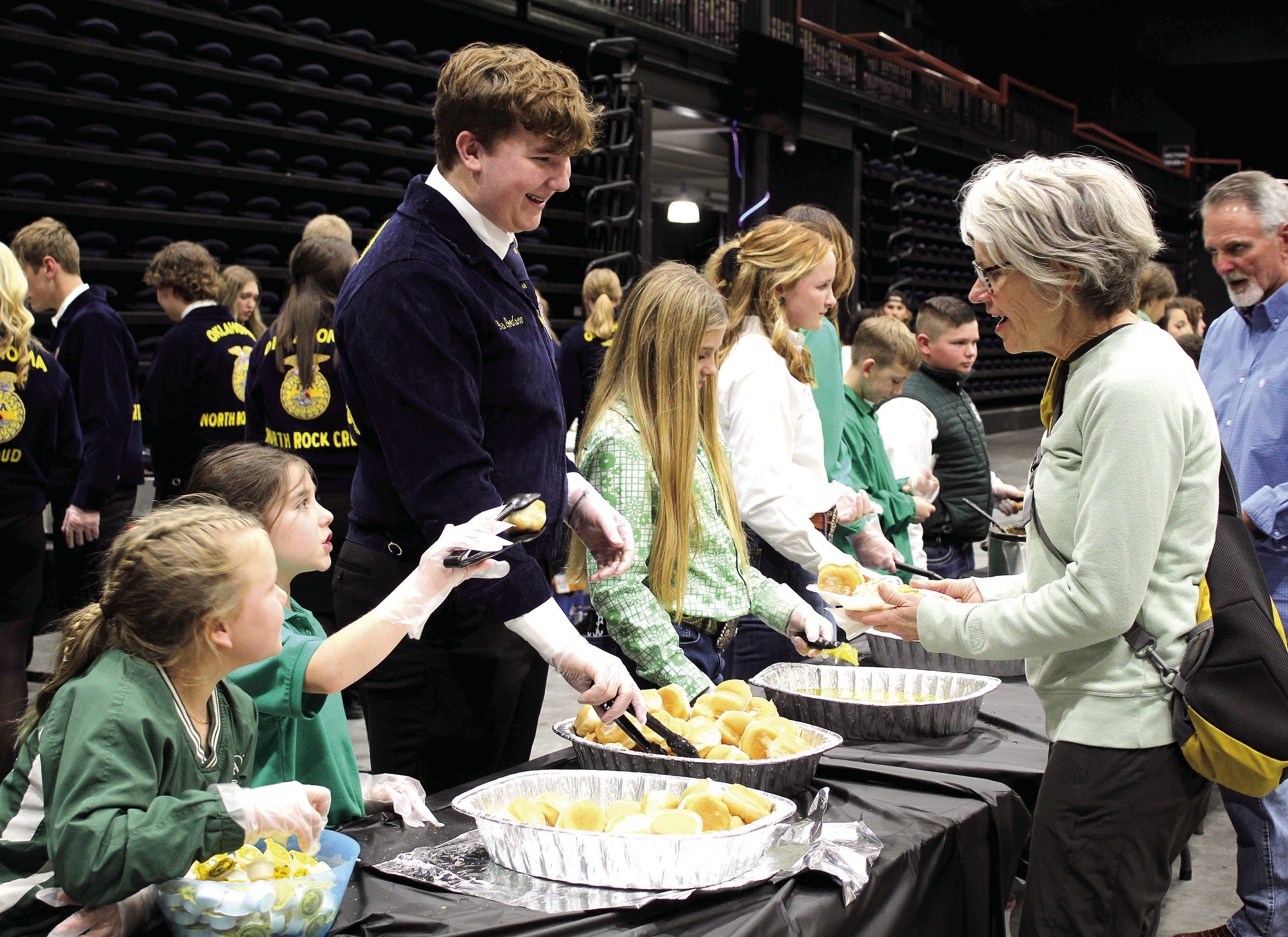 Tecumseh 4-H members Jessi Peacock and Adalyn Seaton and North Rock Creek FFA member Gus Goodson serve Delinda Curtis rolls and butter during the 34th Annual Pottawatomie County Junior Livestock Show Pig Roast and Trophy Auction on Feb. 6. Countywide & Sun/Natasha Dunagan
