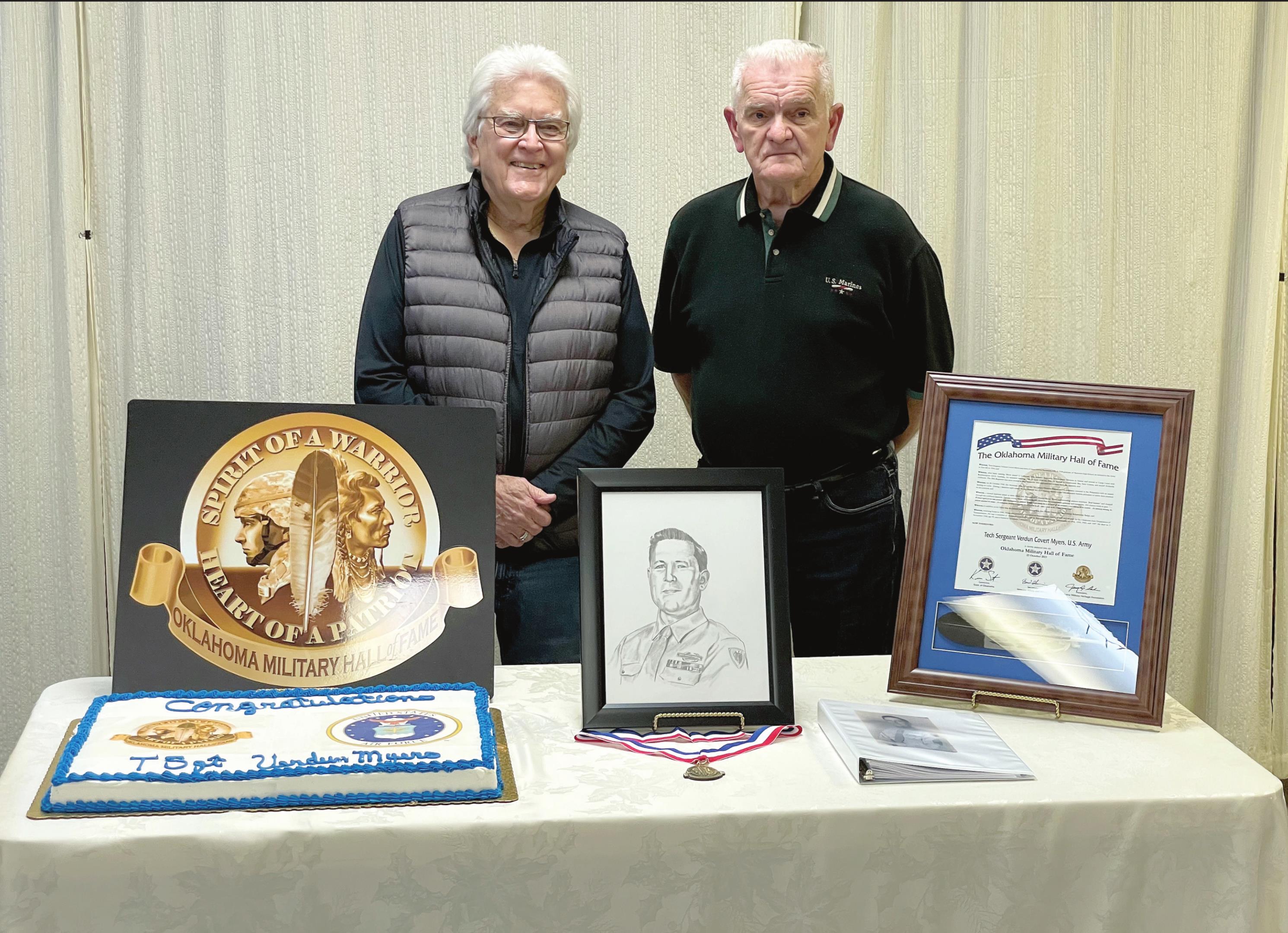 Dr. James Myers, of Tulsa, and Skip Myers, of Tecumseh, pose by a portrait of their father, Tech Sergeant Verdun C. Myers, following a ceremony in which the late WWII veteran was inducted into the Oklahoma Military Hall of Fame. The ceremony was held at American Legion Post 16, in Shawnee, on Dec. 21. Photo provided by OKMHF Ambassador John Farris.
