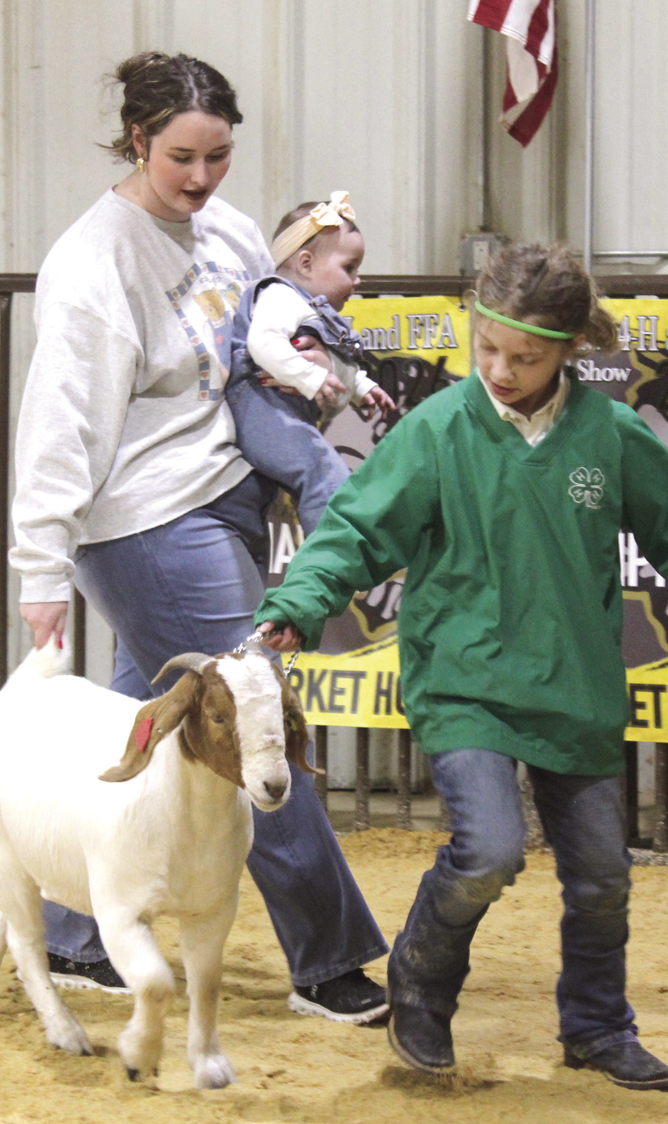 Tecumseh FFA Advisor Mara Carmen holds her baby, Shelby, as she helps 4-H member Aurora Colten to get her goat going.