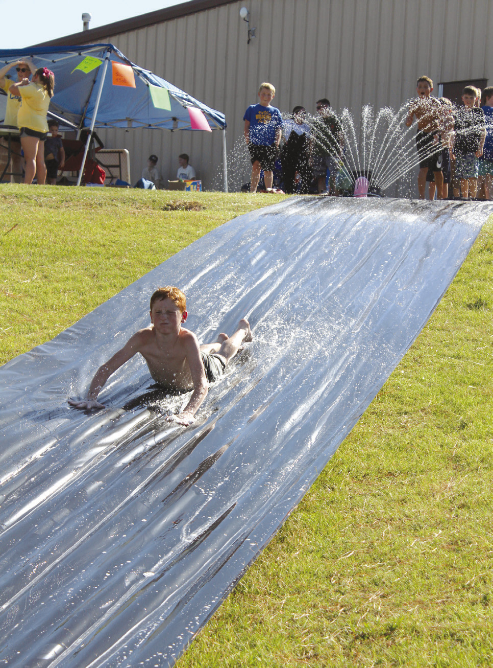 Gunner Billins, 10, of Bethel, cools off on the slip n’ slide, a fund-raiser for the Bethel Little League Cheer program, on Aug. 17. This was one of several booths, including a dunk tank fund-raiser for Bethel Wrestling, at the Bethel High School Blue &amp; Gold Bash held at the football field. Countywide &amp; Sun/Natasha Dunagan