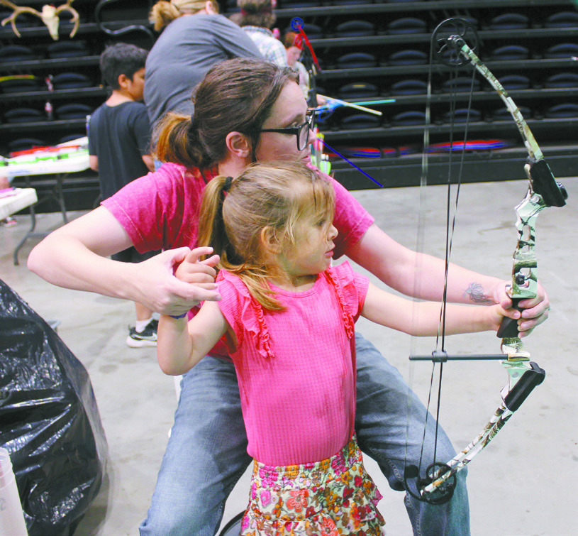 Janilee Marcus, with the Outdoor Nation Expo Youth Archery booth, helps Savannah Morris, 4, of Washington, to shoot a bow for the first time at FireLake Arena on Aug. 9. This is the first year, since the ONE began in 2017, for it to be presented by the Citizen Potawatomi Nation. They also had the Fetch n' Fish Dog Show and Darkwater Adventures Target Bowfishing, as well as an assortment of vendors. Natasha Dunagan, Countywide & Sun