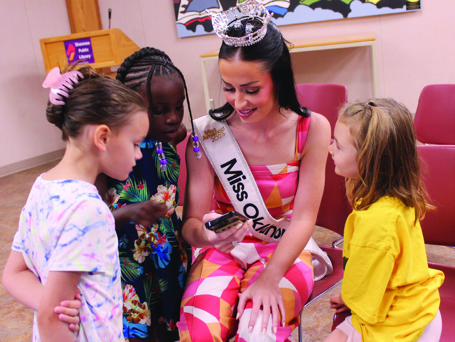 Miss Oklahoma Tessa Dorrell shows a picture of her blue pageant dress to three six-year-olds - Sarah Sprague of Tecumseh, Kenya Lightsey of Shawnee and Sibyl Hays of McLoud - during story time on July 29. Natasha Dunagan, Countywide & Sun