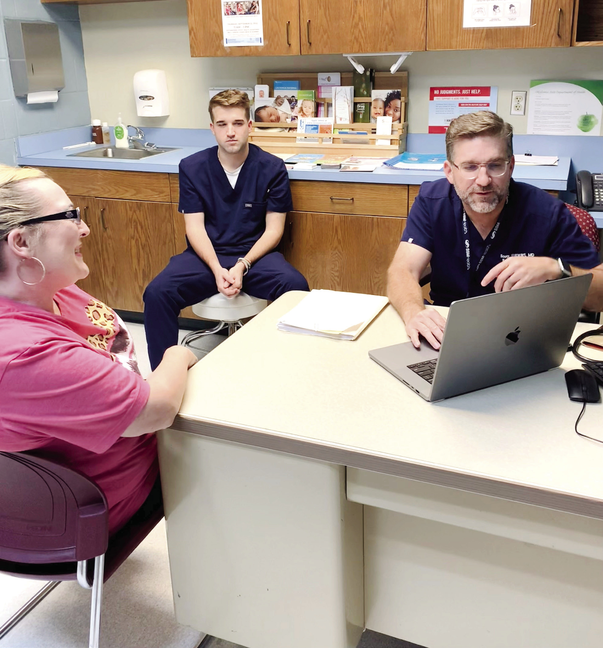 Dr. Scott Stewart talks with Kelly Long, a patient at the Pottawatomie County Volunteer Health Clinic, as his son and medical scribe Parker Stewart looks on, May 11. Stewart also volunteers at the clinic with his other son, Reid, not shown, who screens patients and helps in the pharmacy. Photo provided by Sharon Gerards. 