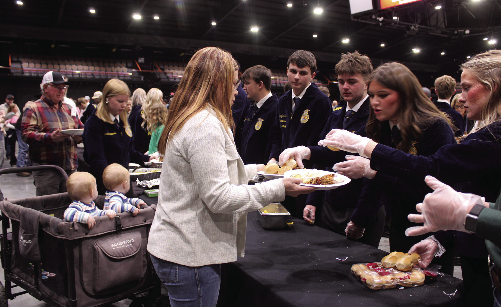 Tecumseh FFA Members Abbi Jordan and Rylee Chaffin add rolls to the plates of Chelsi Peacock, of Tecumseh, as her nine-month-old twins, Gavin and Greyson Pell, sons of Tecumseh FFA Advisor Corey Pell, wait in their cart during the 37th Annual Pottawatomie County Junior Livestock Show (PCJLS) Pig Roast and Trophy Auction, held at FireLake Arena on Feb. 2. Also serving, from left, were Sawyer Spears, Landyn Seaton and Porter Neil. Natasha Dunagan, Countywide & Sun