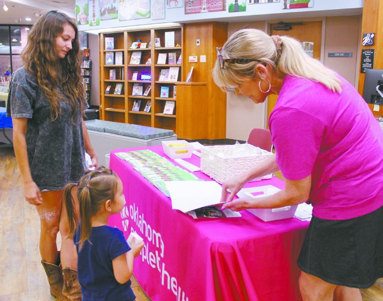Natasha Dunagan, Countywide &amp; Sun Kathy Gooding, Community Relations Coordinator for Oklahoma Complete Health, shows a coloring book to Alice McCathern, 4, of Little Axe, as Tenisha McCathern watches during the event at Shawnee Public Library on Aug. 9. There were about 10 booths with organizations handing out school supplies and free items, in addition to an OBI blood drive.