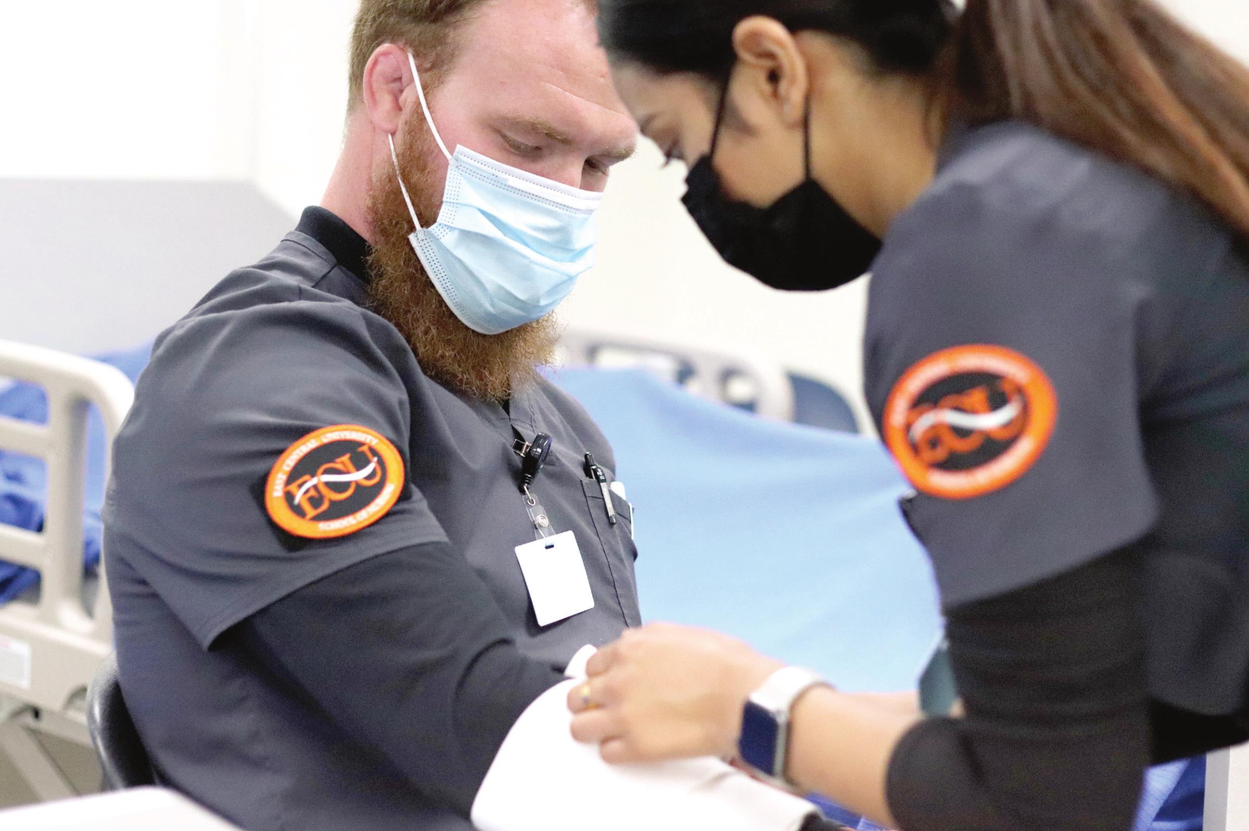 ECU Nursing student Gabriel Rebischke sits patiently while fellow student Suja Shresta practices applying bandages to his arm.