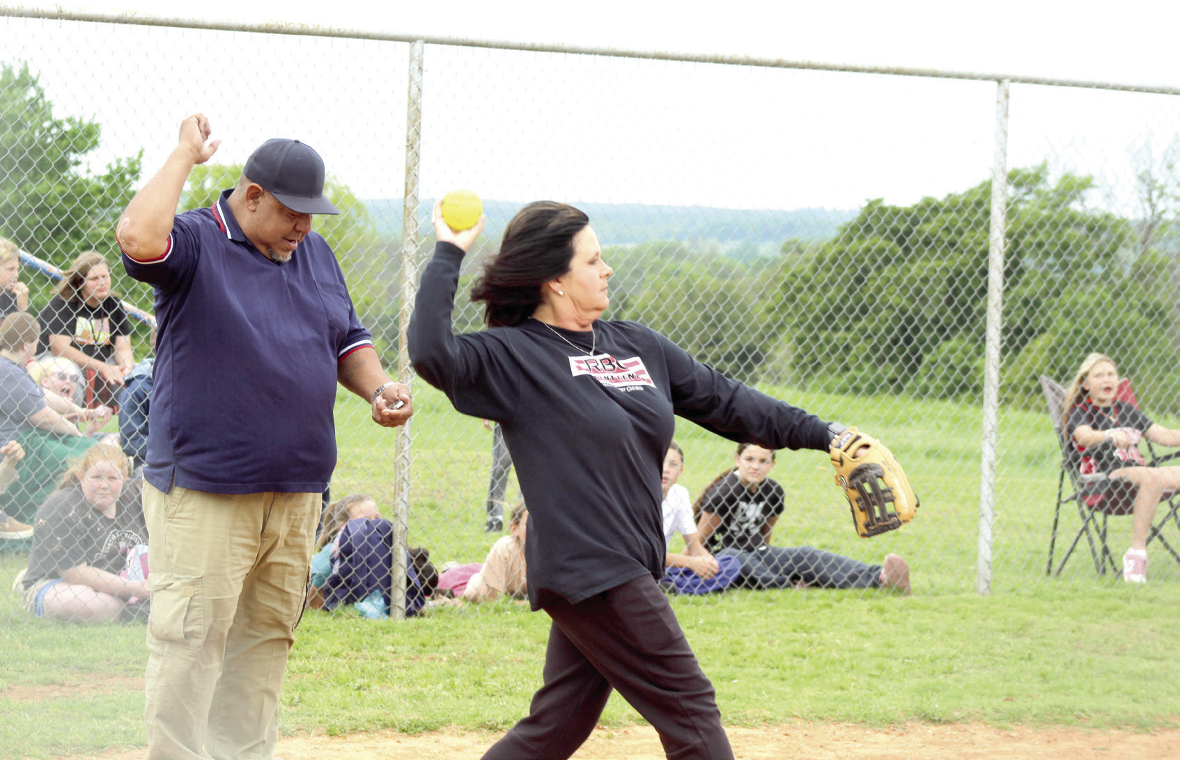 Macomb Fellowship of Christian Athletes leader Helen Lee tosses the ball to the pitcher in her role as catcher during the Macomb Staff vs. Players Game on April 29. Also shown is umpire Eric Thlocco, who was honored during the game for serving as an umpire for 30 years and planning to retire. See more about Thlocco in a future issue of the Countywide & Sun.