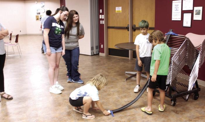 State 4-H STEM Innovators Grace Hobbs and Madison Maddox watch as Caiden Fullbright, 7, Trace Harrington, 7, and Callahan Lemmings, 4, all of Shawnee, test the first step of their roller coaster with a marble. This was at the 'Build It: Roller Coaster' event at Shawnee Public Library on June 16 where they used insulated tubing, masking tape and a cup to build their coasters. The next Build It event will be 'Ready, Set, Blast Off!' on June 30 at 2 pm.