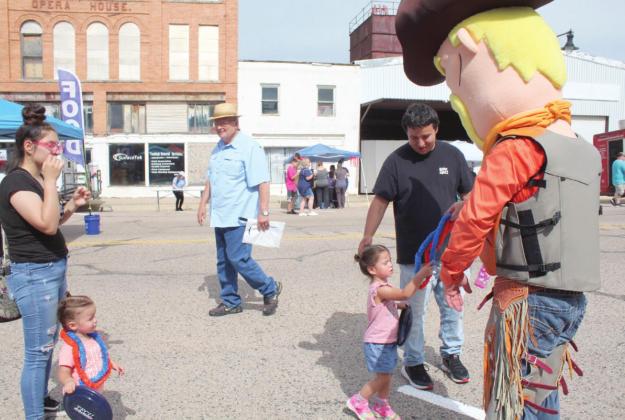 "Cowboy Hank," aka Josh Powell of Cowboys Plumbing, offers plastic leis to Clementine Perez-Enriquez, 2, of Tecumseh, as Briana Perez, Catherine Perez-Enriquez, 1, and Jorge Enriquez look on during the Mingle on Main Street Block Party on June 16. Countywide &amp; Sun/Natasha Dunagan
