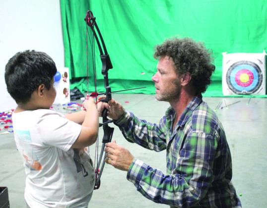Archery Shoot volunteer Harley Coleman teaches Christian Castillo, 7, of OKC, how to shoot a bow during the Outdoor Nation Expo on Aug. 11 at FireLake Arena. The Archery Shoot is organized by the Navarro family of Chandler, said Linet Navarro. Countywide &amp; Sun/Natasha Dunagan