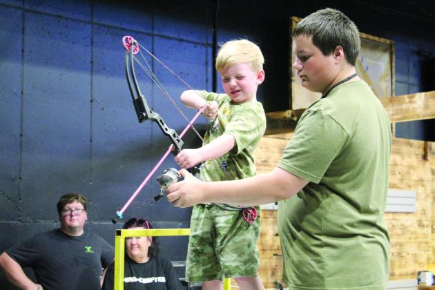 Damian Pearson, 5, of Marlow, is assisted in target bowfishing by Zak McMunn, of Darkwater Adventures in Meeker, during the Outdoor Nation Expo on Aug. 11 at FireLake Arena. Countywide &amp; Sun/Natasha Dunagan