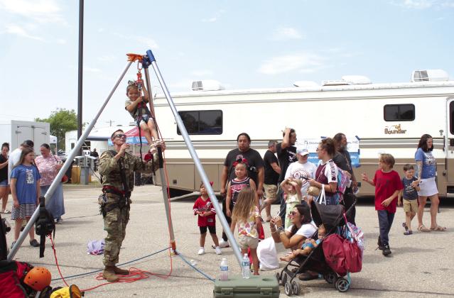 Jolie McFarland, 2, of Wanette, smiles as she is lifted with a harness and pulley by Ron Poland, with the U.S. Army National Guard, at Cops N’ Kids, Aug. 26. The harness was a new attraction this year. Countywide &amp; Sun/Natasha Dunagan