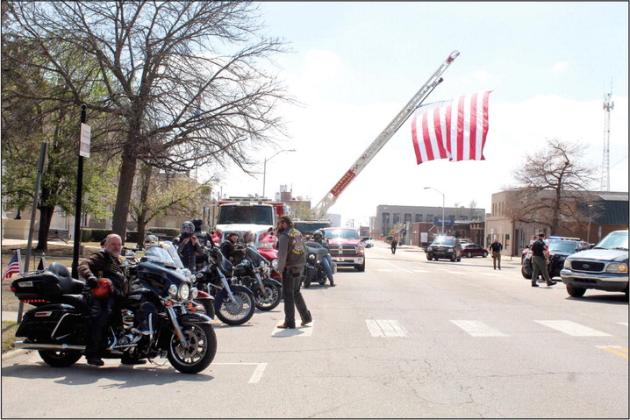 Bikers in the Seventh Annual Ruben Rivers Medal of Honor Ride park in front of the Woodland Veterans Park, March 25, as a 20'x30' U.S. flag hung from a Shawnee Fire Department ladder flies over Broadway Ave. Roll to Wreaths Riders 4 Vets President and Founder Rowdy Butler is shown far left. Countywide &amp; Sun/Natasha Dunagan