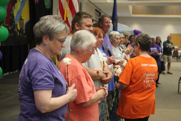 Harriet Byers hands out carnations and passes the microphone to the cancer survivors.