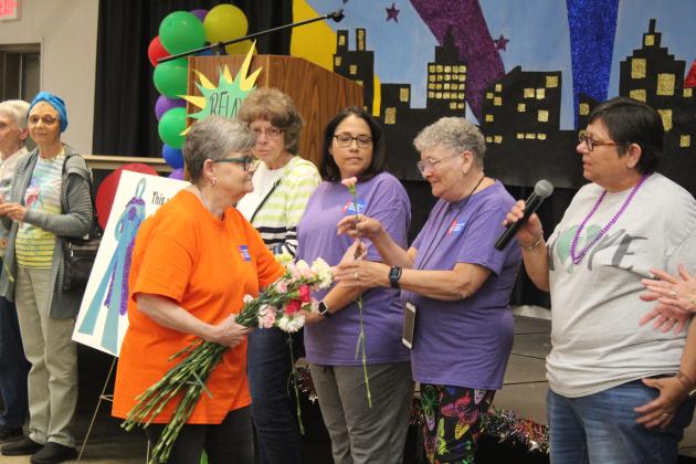Harriet Byers hands out carnations and passes the microphone to the cancer survivors.