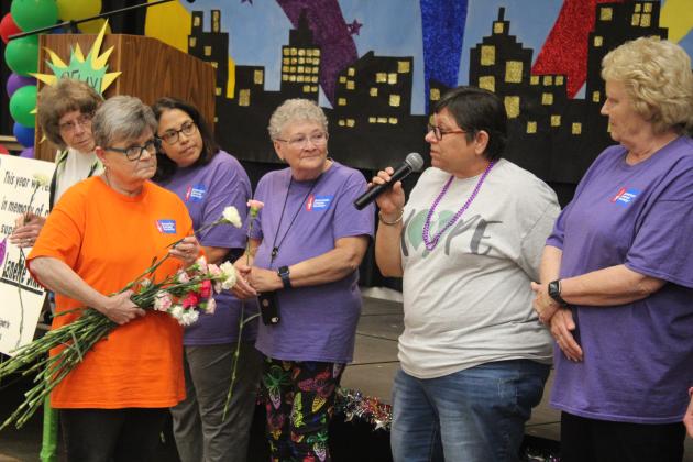 Harriet Byers hands out carnations and passes the microphone to the cancer survivors.