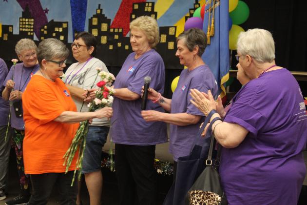 Harriet Byers hands out carnations and passes the microphone to the cancer survivors.