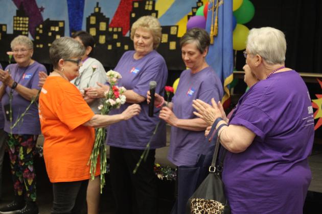 Harriet Byers hands out carnations and passes the microphone to the cancer survivors.