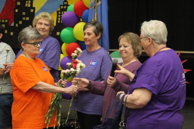 Harriet Byers hands out carnations and passes the microphone to the cancer survivors.