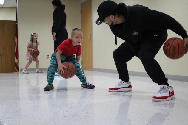 Potawatomi Fire point guard Tevin Foster, far right, shows Kamden Bates how to do a figure eight around his legs with a basketball, as shooting guard Deon Lyle coaches Peyton Kirkpatrick on dribbling, at the Shawnee Early Childhood Center on April 27.