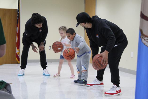 Potawatomi Fire shooting guard Deon Lyle, far left, and point guard Tevin Foster, far right, teach Stevie Lunsford and Andy Lira-Molina to dribble at the Shawnee Early Childhood Center on April 27. Four members of the team visited the center where they worked on dribbling with six students selected from the audience, advised them to listen to their teachers and parents, posed for pictures with each class, signed autographs, and handed out tickets to a Fire game. Countywide &amp; Sun/Natasha Dunagan