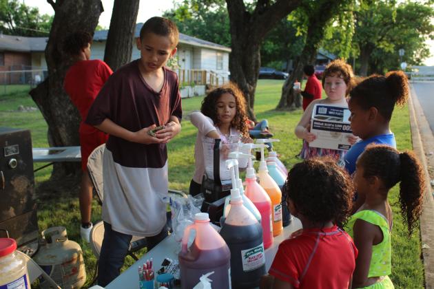 Kash Tillis, 9, and Makayla Tillis, 10, serve snowcones to children during "The Block is Hot: Live Music Block Party" on May 28 in the Dunbar Heights neighborhood of Shawnee. They are the grandchildren of Remetia Tillis who owns "Two Chicks Cookin'" food truck.