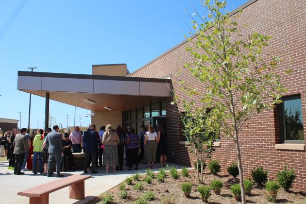 People gather for the ribbon cutting at Sycamore cottage, as a sycamore tree is shown planted in front of the residential building.