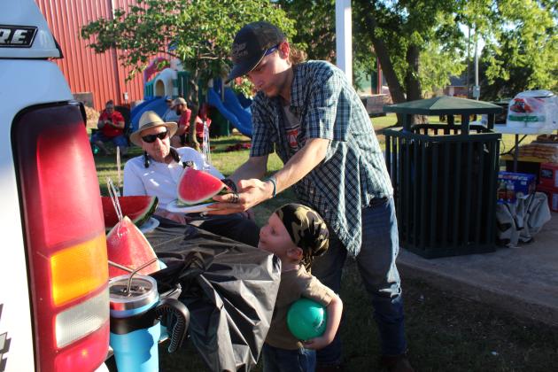Trentin Collett selects a slice of watermelon for Zackary Collett, 2, both of Wanette, as Lions Club member Jerry Bourassa looks on. Bourassa has brought watermelon to give away at the Wanette Independence Day event for several years. Countywide &amp; Sun/Natasha Dunagan