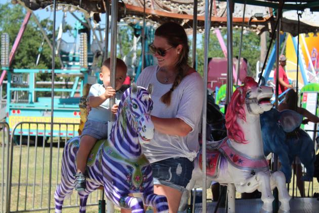 Heather Belt holds onto 8-month-old Chloe Belt as she rides a purple zebra on the carousel at the McLoud Blackberry Festival on July 9. Countywide &amp; Sun/Natasha Dunagan