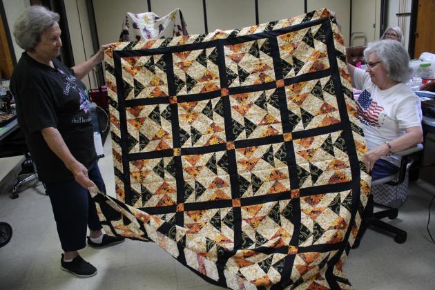 Judith Branson and Ann Cosgrove hold up a quilt top which was completed as a joint effort by the Spinning Spools Quilt Guild.