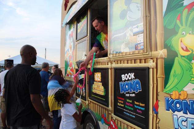 Co-owner Aron Sanders hands Nedra Edwards, 6, of Tecumseh, a plastic lei from the Kona Ice of Shawnee truck at FireLake Casino on July 3.