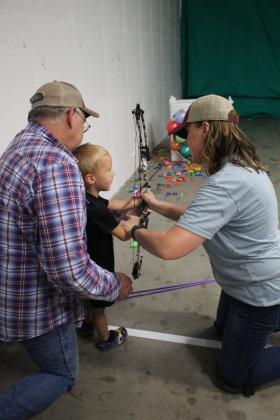 Tommy Fugate, 3, of Macomb, gets archery instruction from Linet Navarro, of Chandler, and the support of his "Poppy," Jeff Fugate, during the Outdoor Nation Expo on Aug. 13. Navarro brought four archery targets and set up for kids of all ages at FireLake Arena. Countywide &amp; Sun/Natasha Dunagan