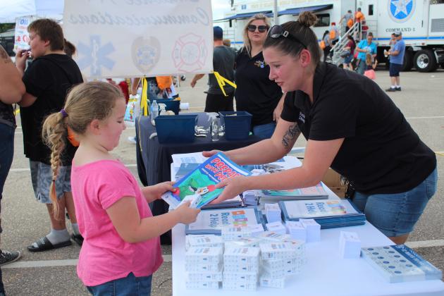 Shawnee Emergency Director Rachelle Erickson offers a coloring book to Lexi Igo, 7, of McLoud, at Cops n' Kids on Aug. 27 at the Heart of Oklahoma Expo Center. Countywide &amp; Sun/Natasha Dunagan