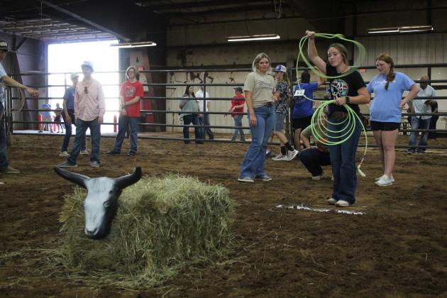 Emma Bellah, of McLoud FFA, tries her hand at roping a dummy steer, as fellow chapter member Austyn Wood, left, and Sydney Murray, of Bethel FFA, look on during the individual events of the 13th Annual Farmhand Olympics on Sept. 7. Part of the Pottawatomie County Free Fair, the event also offered watermelon seed spitting, horseshoes, and bolt block, followed by the team relay races. Countywide &amp; Sun/Natasha Dunagan