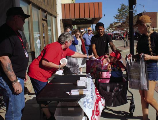 Toys for Tots coordinator for Pottawatomie, Lincoln, and Seminole counties, Denise Vernon, hands out plastic cups to a princess and Mario, as Jon Vernon (far left) looks on, during trick-or-treating at Monsters on Main in downtown Shawnee, Oct. 22.  Denise Vernon said this will be the first year that donations in her coverage area will stay in the area. Countywide &amp; Sun/Natasha Dunagan