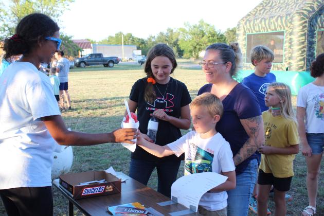 Macomb freshman McKenzie Brummett hands a snowcone to Christopher Kearby, 7, of Macomb, as Kayla Hatler and Jenelle Kearby look on during Macomb Trade Days on Sept. 23. Proceeds from snowcone and candy sales benefitted Macomb High School Athletics.