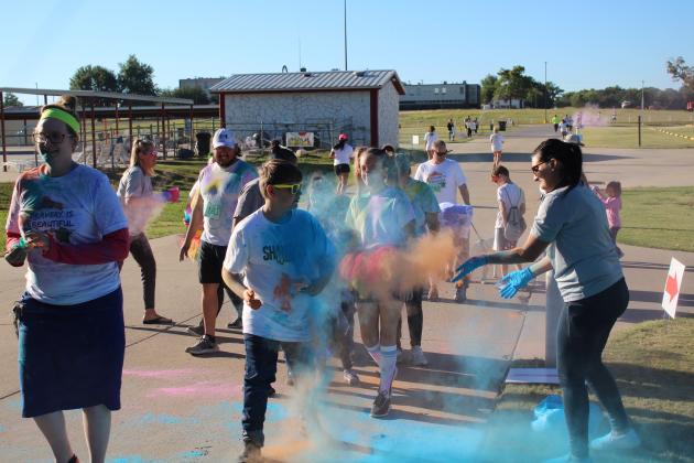 At one of six color stations, Whitney Coots, far right, and Deanna Voeks, left with cup, both of CPN Indian Child Welfare, sprinkle colored powder on some of the House of Hope Color Fun Run participants on Oct. 1 at the CPN Festival Grounds. Event organizer, Kayla Woody, said there were 135 participants signed up online and more who entered on that day. Countywide &amp; Sun/Natasha Dunagan