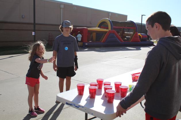 Harper Orso, 6, tries her hand at the ball toss as Shawnee wrestlers Cooper James and Benjamin Cole look on during the Shawnee Wrestling Carnival on Oct. 13 at Shawnee High School.