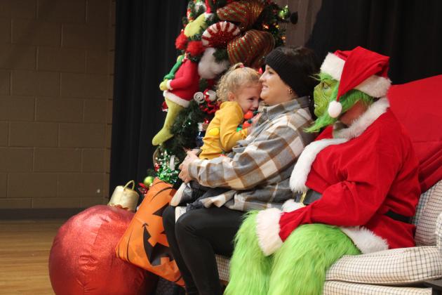 Emery Thomas, 2, peeks at the Grinch from the safety of her mom, Catye's arms while getting their picture taken by Jerilyn Hart with the Tecumseh Public Library. Free photos with the Grinch, free cocoa, crafts, games and face painting were available in "Whoville" at the Tecumseh City Hall Auditorium on Dec. 8. Countywide &amp; Sun/Natasha Dunagan