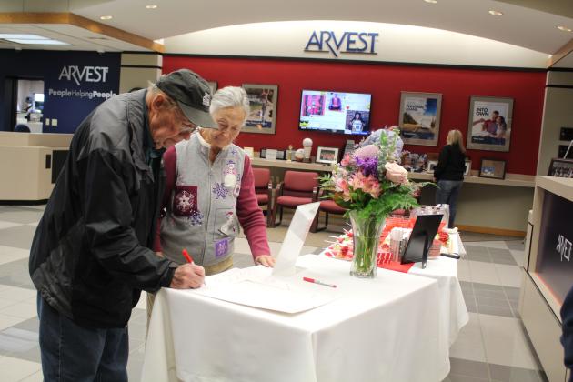 Jay Tabor signs a frame, as Pat Tabor looks on during Kim Rawls' retirement reception held at the downtown Shawnee Arvest branch on Dec. 30. Arvest Community President Brian Nave said 138 people signed the frame for Rawls who retired after 43 years. Countywide &amp; Sun/Natasha Dunagan